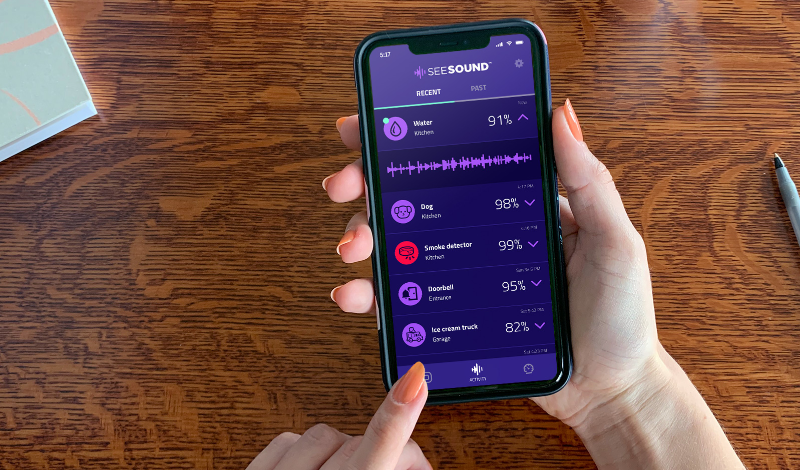 SEE SOUND app activity screen shown on phone in hands with desk supplies in background